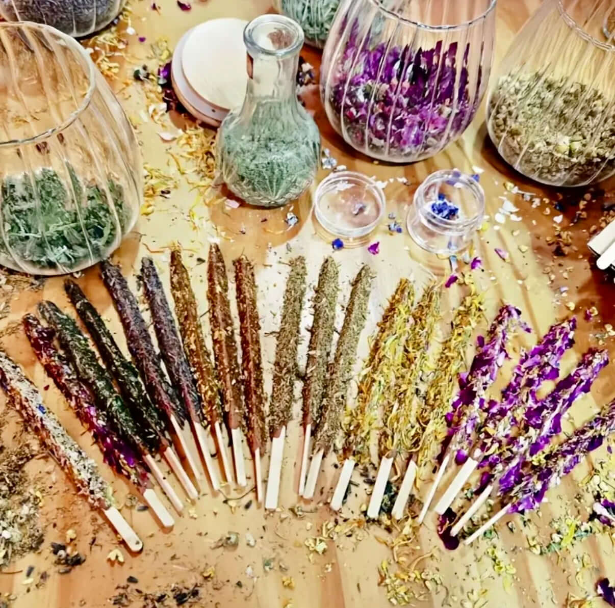 Artisan Dipped Palo Santo Ritual Sticks arranged on a wooden table with jars of herbs and flowers in the background.